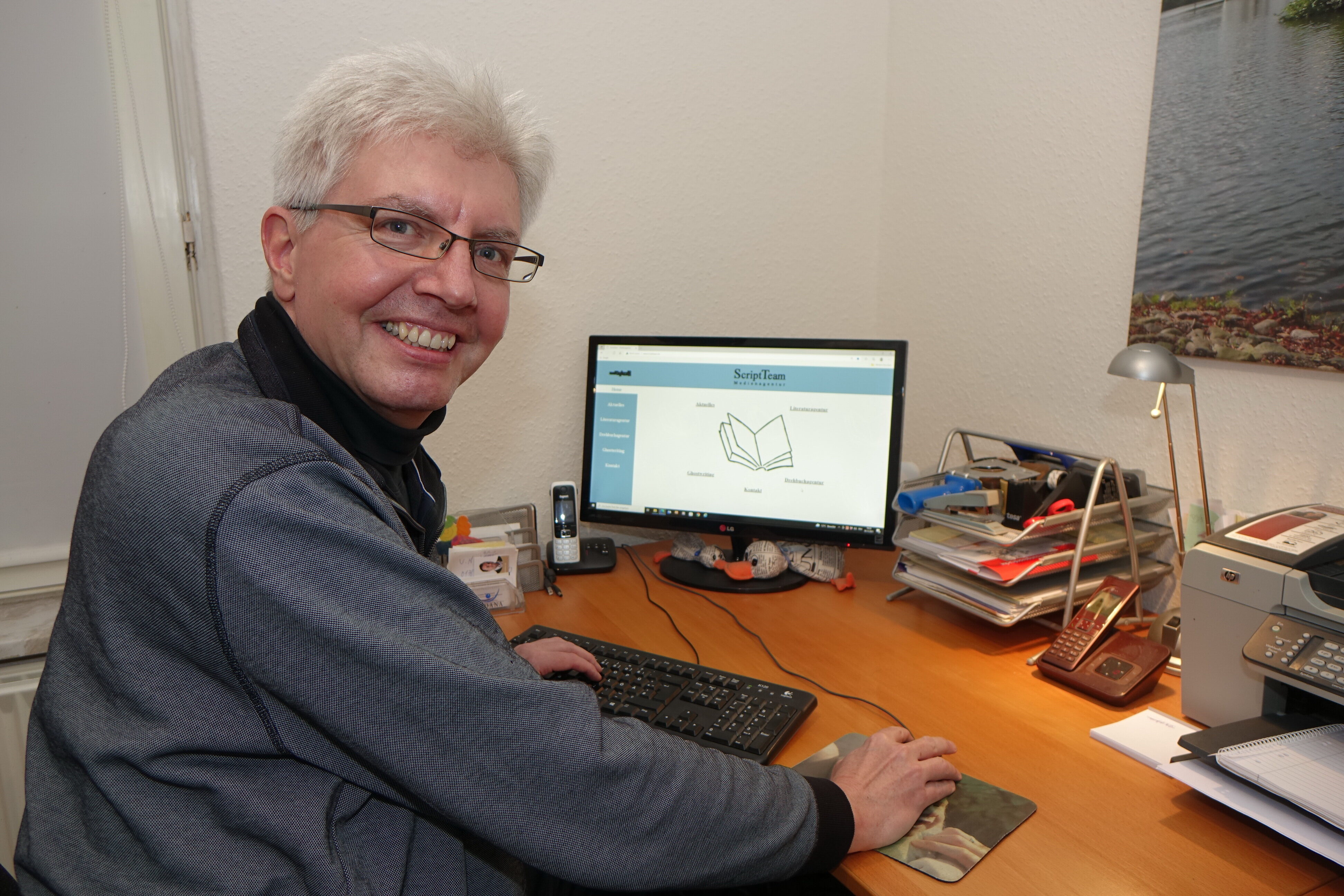 Carsten Wittmaack sitzt an seinem Arbeitsplatz und lächelt in die Kamera