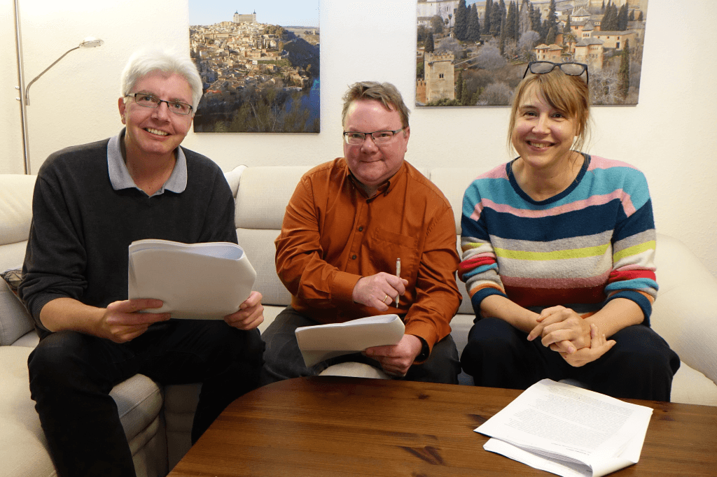 Carsten Wittmaack (links), Sönke Rothers (mitte) und Nicole Wollschlaeger (rechts) sitzen mit finalem Manusscript auf einer weißen Couche